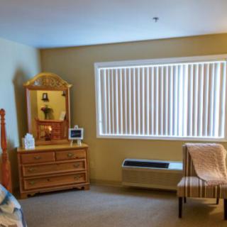 A tidy bedroom with a dresser, mirror, and large window with blinds.
