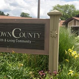 Community sign with surrounding greenery and a building in the background.