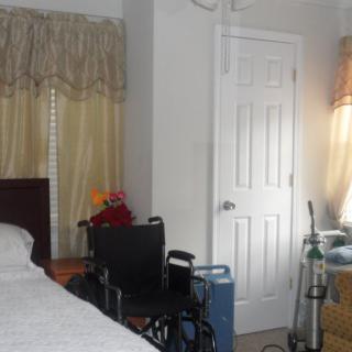 A bedroom with a bed, wheelchair, and curtains near a closed door.