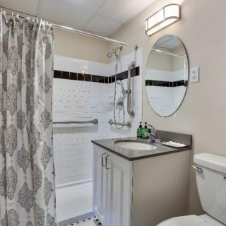 A modern bathroom with a shower curtain, sink, circular mirror, and toilet.