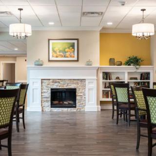 A modern dining area with wooden floors, featuring tables and chairs, a fireplace framed by built-in shelving, and elegant lighting fixtures.