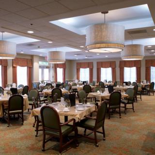 An elegantly set dining room with multiple tables and chairs, featuring soft lighting and a welcoming atmosphere.