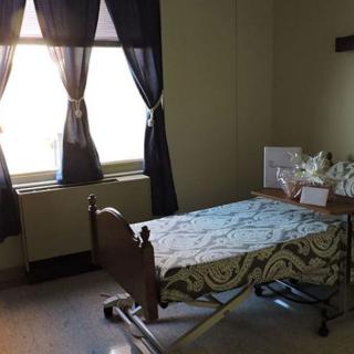 A quiet hospital room with an empty bed and sunlight streaming through the curtains.