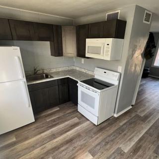 A modern kitchen featuring dark cabinets, a white refrigerator, stove, and microwave with wooden flooring.