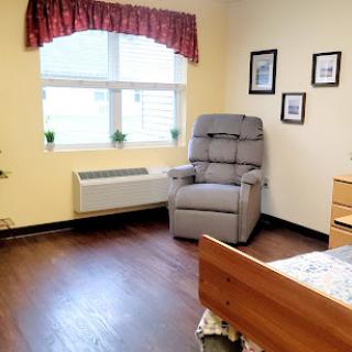 A cozy room featuring a bed, a chair, and natural light streaming through the window.