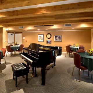 A cozy room featuring a grand piano, surrounded by tables and chairs with warm lighting.