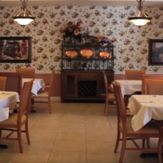 A cozy restaurant interior with tables and chairs arranged neatly, decorated with floral wallpaper and dim lighting.