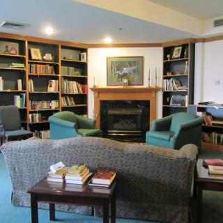 A cozy library reading area with bookshelves surrounding a fireplace and comfortable seating.