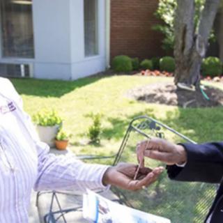 Two people exchanging items while shaking hands outside.