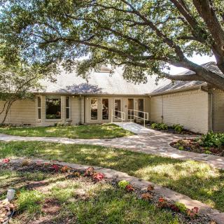 A single-story house with a large tree in the front yard and a winding pathway leading to the entrance.