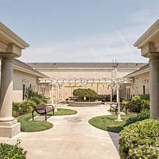A serene courtyard with benches, surrounded by greenery and classical architecture.