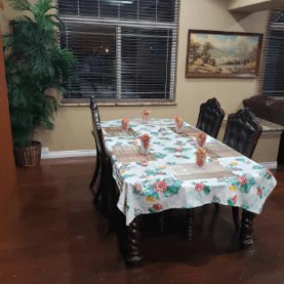A dining room with a table covered in a floral tablecloth and surrounded by chairs.