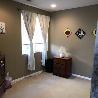 A cozy bedroom with a dresser, lamp, and decorative wall art.
