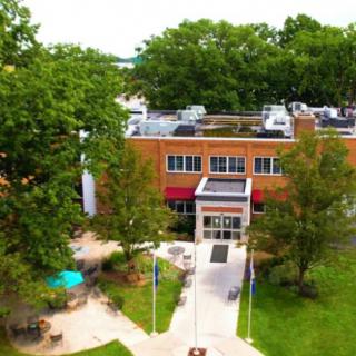 Aerial view of a brick building surrounded by trees with a pathway leading to the entrance.
