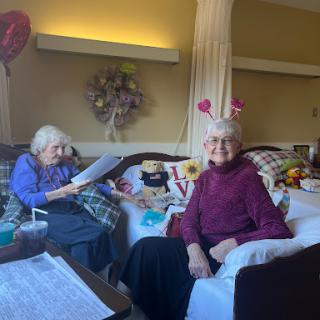 Two elderly friends enjoying time together in a cozy setting, surrounded by decorations and warmth.