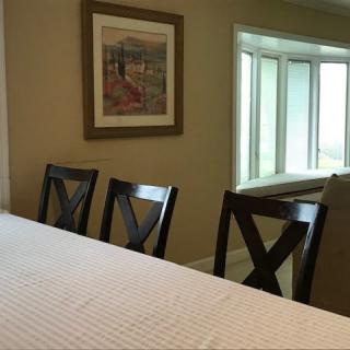 A dining room with a table, chairs, and a window featuring a hanging painting.