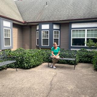 A person sitting on a bench in a garden area outside a building.