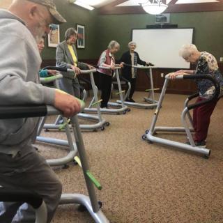 A group of seniors participating in an indoor exercise class using support frames.