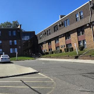 A view of a residential apartment complex with a parking area on a sunny day.