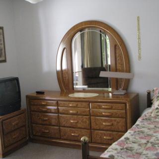 A bedroom with a wooden dresser and mirror, a television, and a floral bedspread.