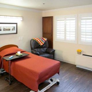 A cozy room with a hospital bed, leather chair, and a window dressed in shutters.