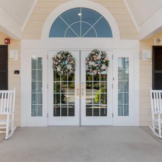 A welcoming entrance featuring double glass doors adorned with wreaths, flanked by white rocking chairs.