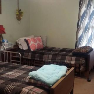 A cozy bedroom with two single beds, plaid bedding, and a lamp by the window.