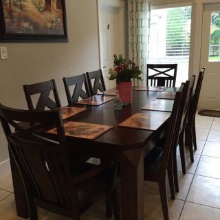 A dining room with a large wooden table set for eight, featuring placemats and a floral centerpiece.