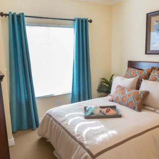 A cozy bedroom with a neatly made bed, adorned with decorative pillows, and teal curtains framing the window.