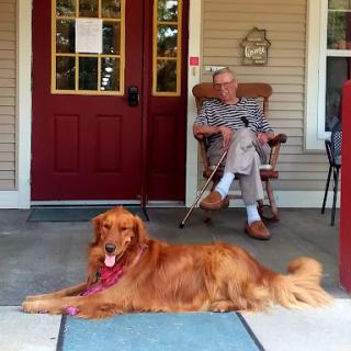 An elderly man enjoying a peaceful moment on the porch with his golden retriever lounging beside him.