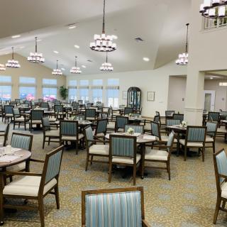 A spacious dining room with neatly arranged tables and chairs, featuring elegant lighting fixtures.