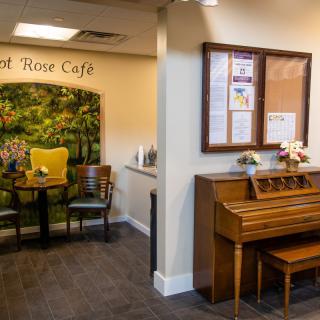 A cozy indoor cafe setting featuring a piano and a small seating area with chairs and a table.