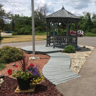 A quaint gazebo with a winding wooden walkway surrounded by landscaped plants and flowers.