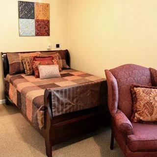 A cozy bedroom interior featuring a bed with patterned bedding and an armchair.