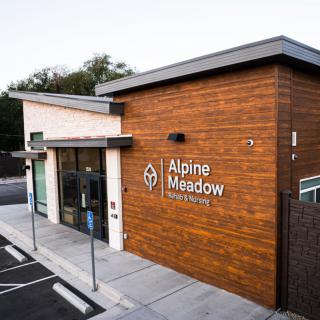 A modern storefront with wood paneling and a clear sign, surrounded by a small parking area.