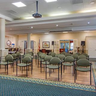 An indoor meeting room with rows of chairs facing a stage area and a projector hanging from the ceiling.