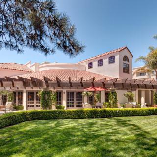 A beautiful house with Mediterranean architecture surrounded by lush greenery and a well-maintained lawn on a sunny day.