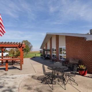 A sunny outdoor patio with seating, a pergola, and an American flag near a brick building.