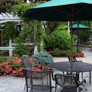 A serene outdoor patio setting with a table, chairs, and vibrant flowers surrounded by lush greenery.