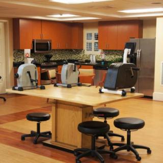 A multifunctional therapy room with kitchen facilities and exercise equipment.