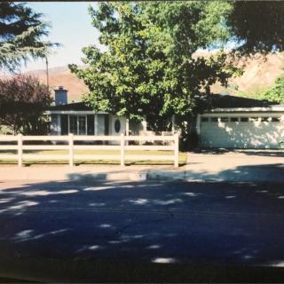 A suburban house with a white fence and surrounding trees.
