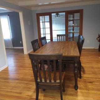 A dining room with a wooden table and chairs, featuring a polished wooden floor and glass-paned doors.