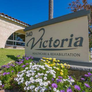 A sign for Victoria Health Care & Rehabilitation in front of a building with colorful flowers.