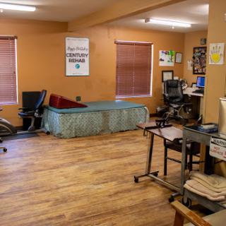 An organized workspace with a bed, desk, and chairs in a well-lit room.