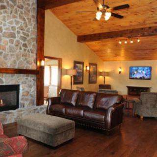 A cozy living room with a fireplace, leather couches, and a wood-paneled ceiling.