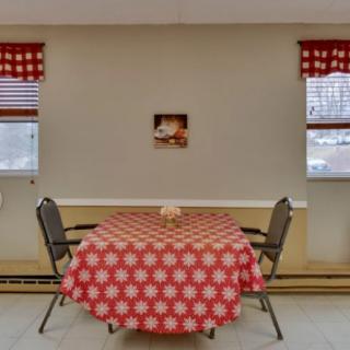 A cozy dining area with a red checkered tablecloth and two chairs, flanked by windows with matching curtains.