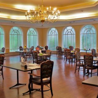 An elegant dining room with large windows and a chandelier, featuring several tables and chairs.