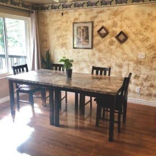 A cozy dining room with a wooden table and chairs, decorated with wall art and a potted plant by the window.
