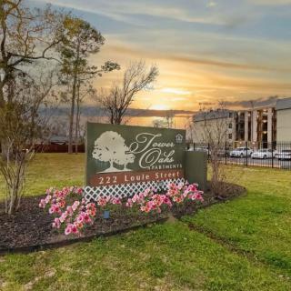 A landscaped entrance sign with flowers, set against a sunset backdrop and nearby buildings.