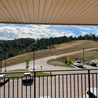View from a balcony overlooking a winding road with cars, surrounded by trees and a partly cloudy sky.